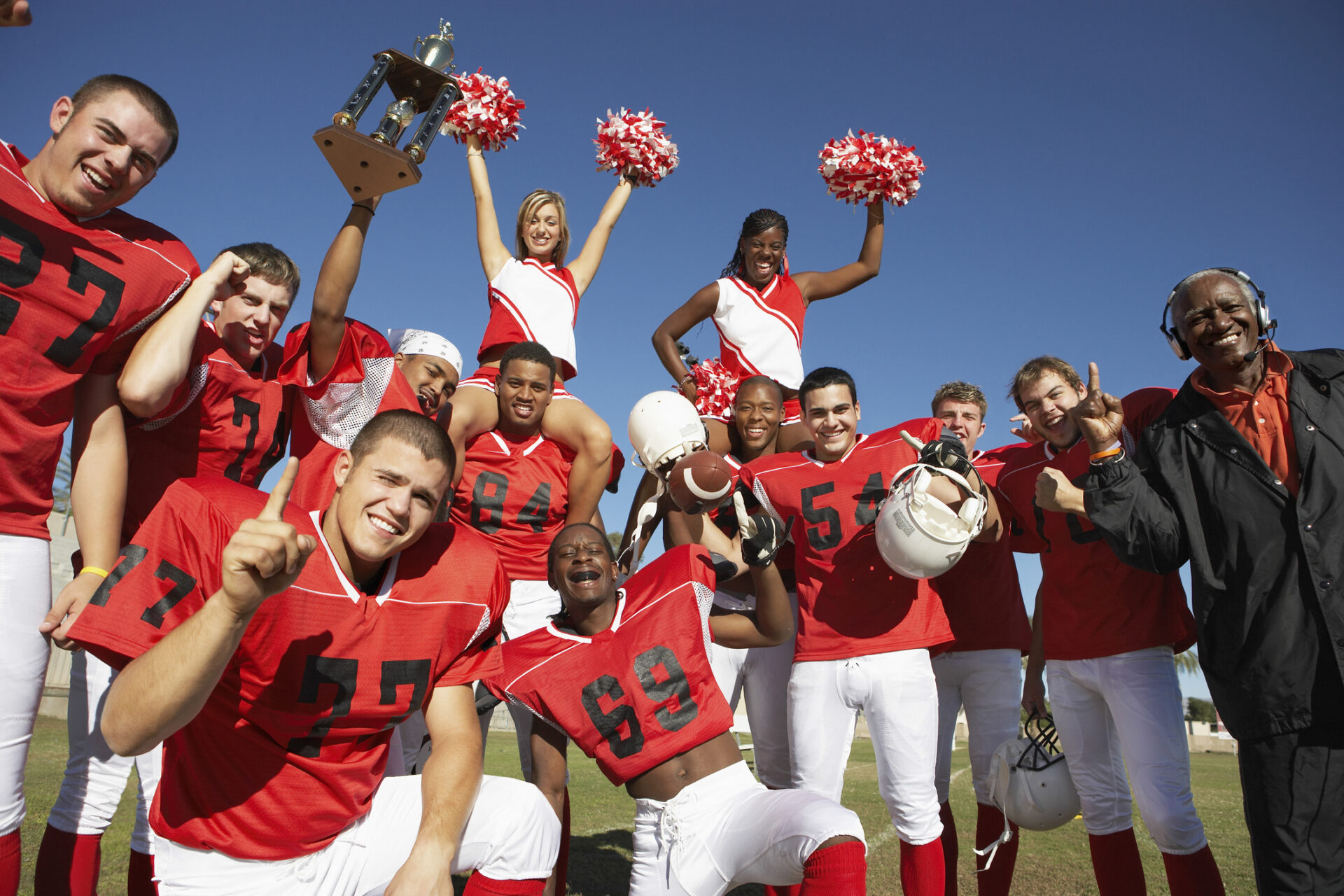 Football Team With Cheerleaders And Coach Celebrating Success On